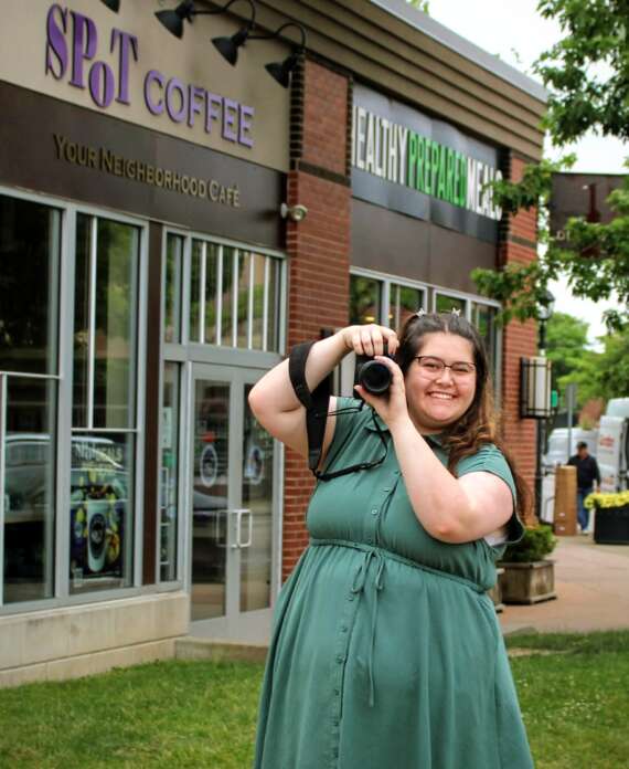 Image of Rebecca Nagel holding up a camera in front of 2 local businesses in Kenmore.