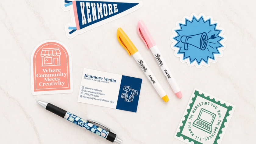 Flat lay of Kenmore Media marketing materials including business cards, branded stickers, and pens arranged on a light marble surface, representing affordable social media marketing and content creation services for small businesses in Buffalo, New York.