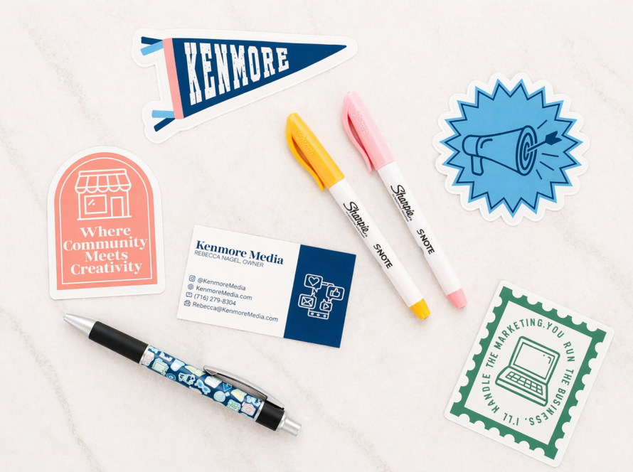 Flat lay of Kenmore Media marketing materials including business cards, branded stickers, and pens arranged on a light marble surface, representing affordable social media marketing and content creation services for small businesses in Buffalo, New York.